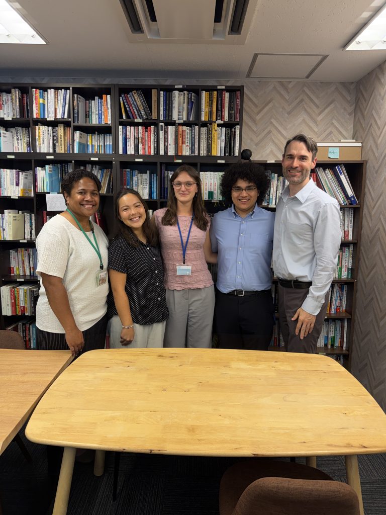 Micah standing in front of a table with four other people posing for the camera