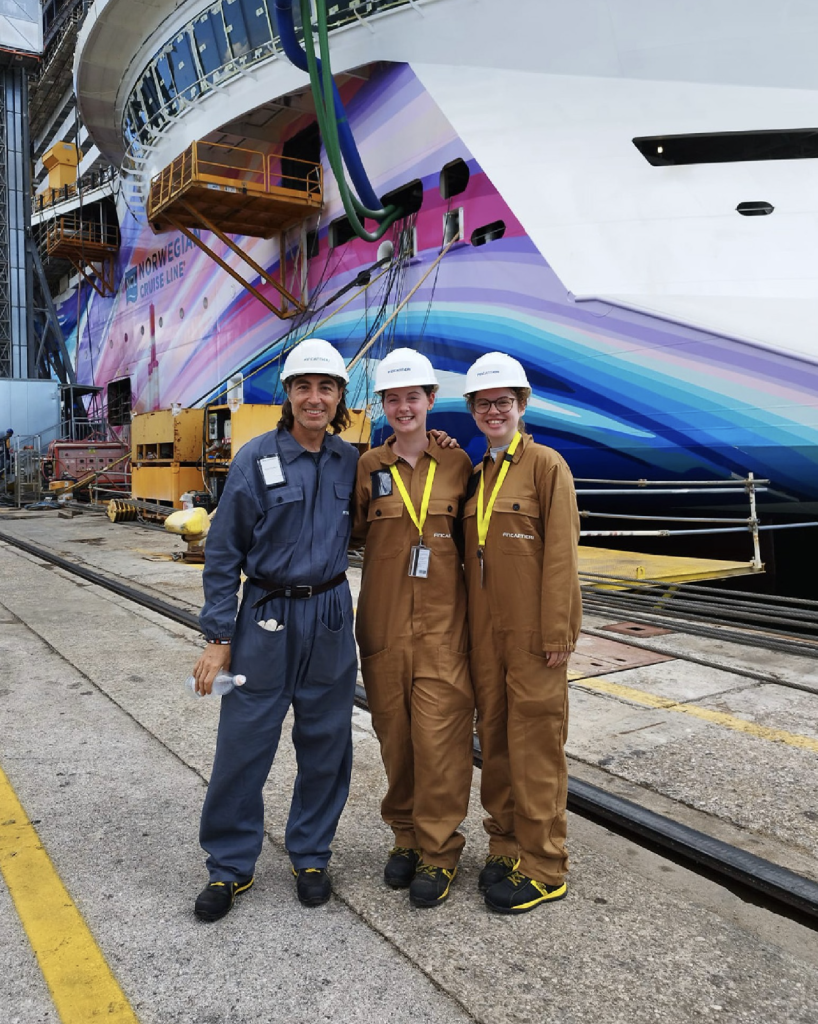 Katie Axelsen standing with two others in front of a ship